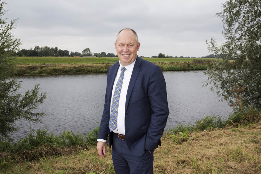 Bert Boerman in blauw pak met stropbos tegen de achtergrond van een rivier