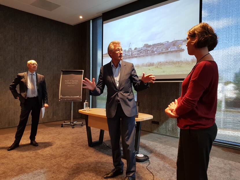 Twee mannen en een vrouw in gesprek tegen de achtergrond van een beamerscherm