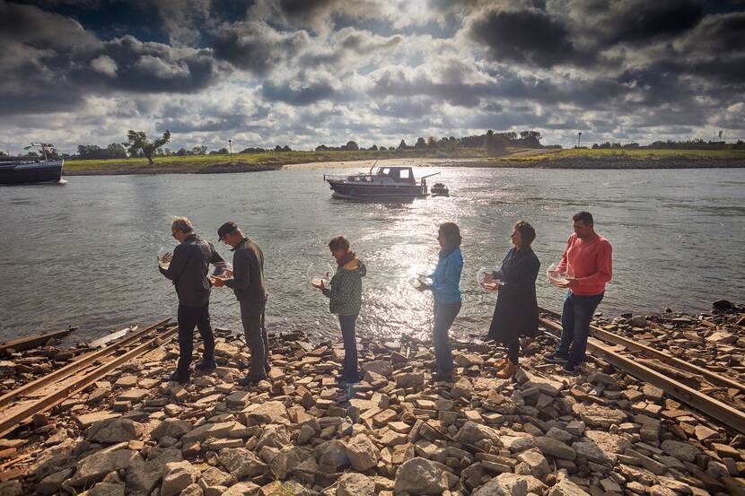 Mensen met vissenkommen aan een stenige rivieroever.