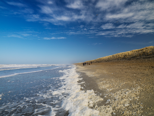 Strand met zee, schuimkoppen en blauwe lucht met dunne bewolking