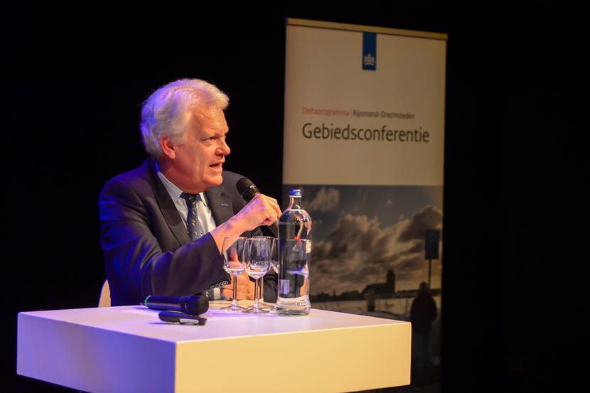 Deltacommissaris Wim Kuijken met een microfoon in zijn hand achter een tafel.