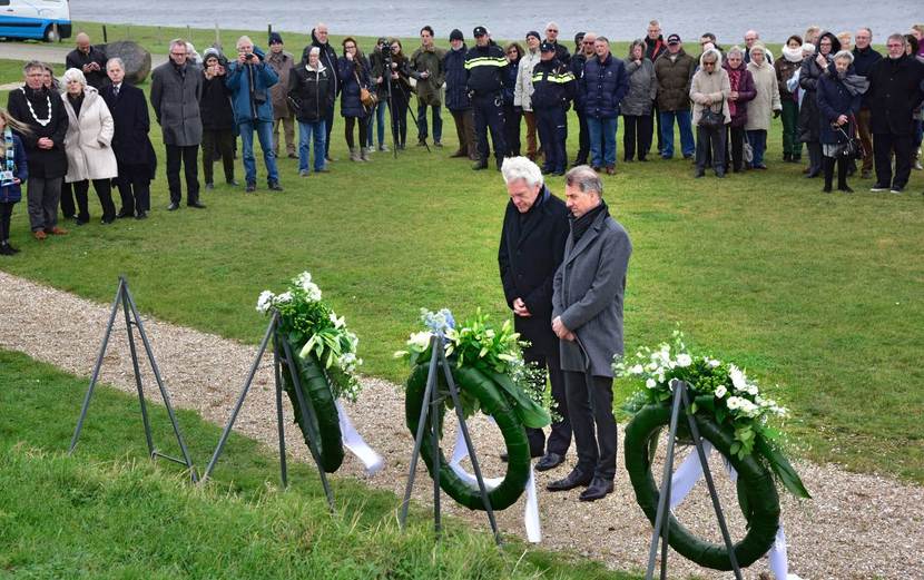 Groep mensen in halve cirkel rondom drie herdenkingskransen