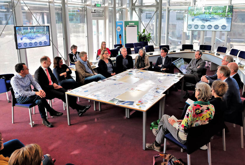 Overleg tijdens werkbezoek rond een tafel, er worden tekeningen bekeken