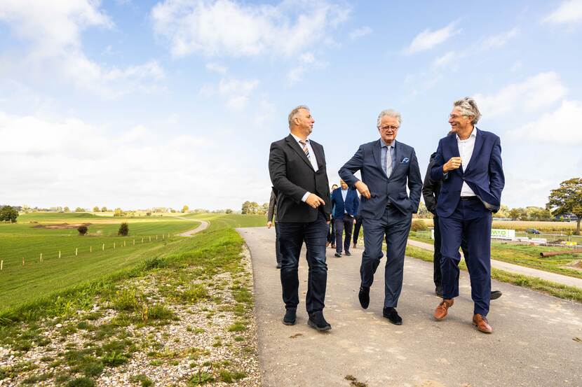 Drie mannen in pak lopen over een winderige dijk