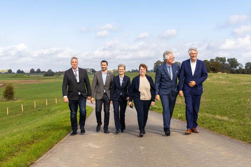 Zes net geklede mensen lopen over een weg omhoog richting de camera.