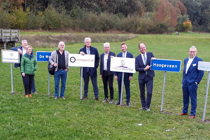 Deltacommissaris Peter Glas en diverse andere mensen staan bij bordjes op palen in een weiland